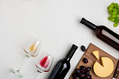 Two wine glasses with red and white wine,bottles of red wine and white wine, cheese on white background. Horizontal view from the top