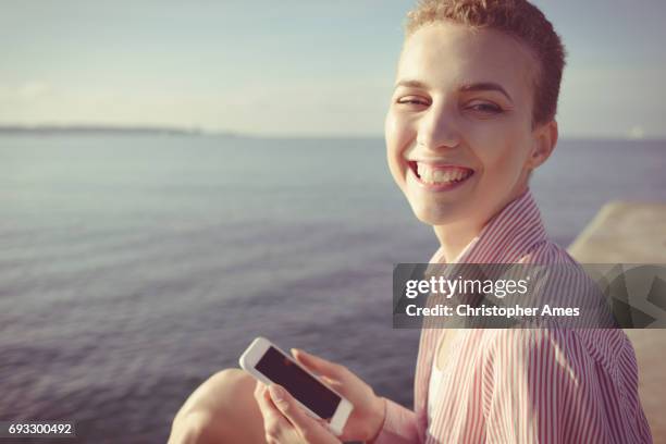 so happy using mobile phone at the seaside - androgynous people stock pictures, royalty-free photos & images