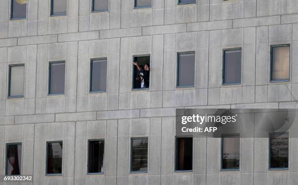 An Iranian policeman holds a weapon as another one gestures from a window at the Iranian parliament in the capital Tehran on June 7, 2017 during an...