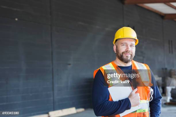 worker in safety vest and hardhat holding digital tablet - laborer stock pictures, royalty-free photos & images