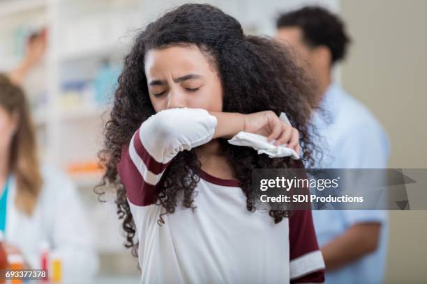 mixed race preteen girl sneezes into her arm - tossir imagens e fotografias de stock