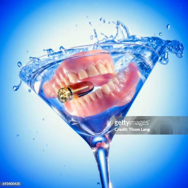 false teeth biting a bullet in a cocktail glass - leuchtgeschoss stock-fotos und bilder