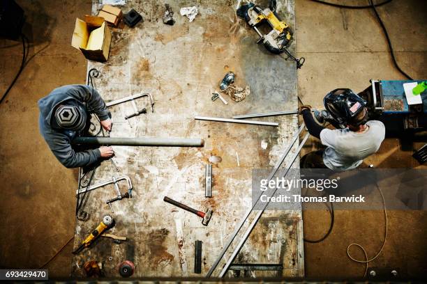 overhead view of men working on project at bench in metal workshop - welding mask stock pictures, royalty-free photos & images