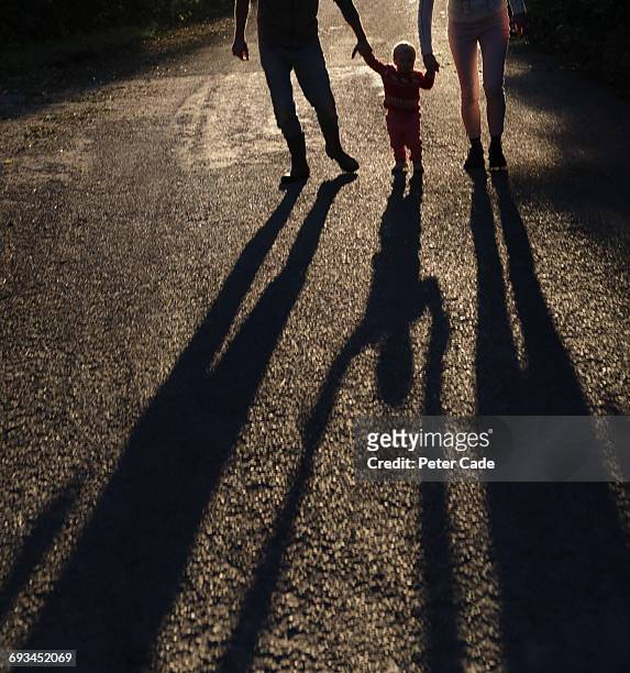 family walking holding hands, long shadows - three people silhouette stock pictures, royalty-free photos & images