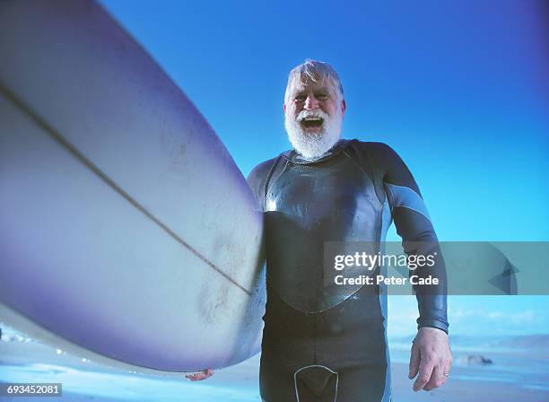 older man on beach holding surfboard - jeune d'esprit photos et images de collection