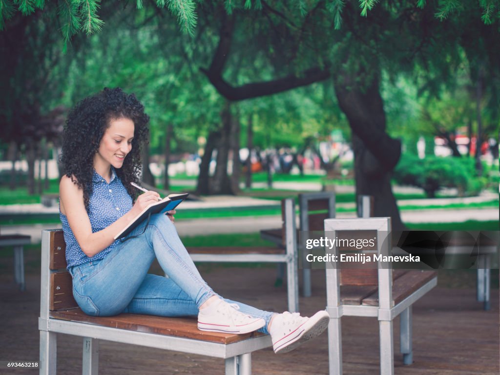 Young woman sitting on a bench and writing notes in notebook