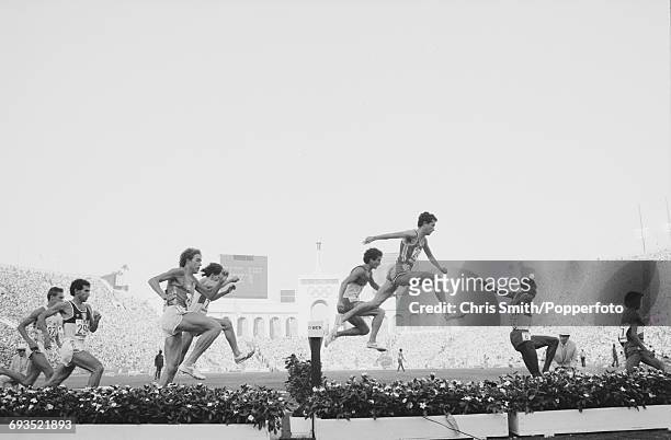 View of athletes clearing the water jump hazard during competition in the Men's 3000 metres steeplechase event, with Roger Hackney of Great Britain...