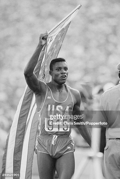 American athlete Carl Lewis celebrates with the United States national flag after finishing in first place with a time of 9.99 seconds to win the...