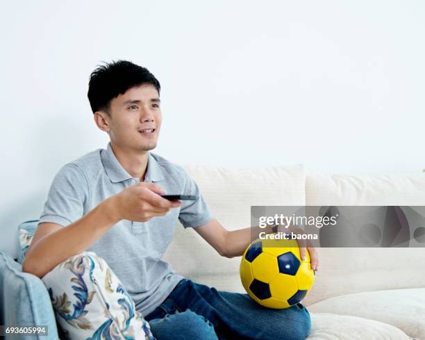 man watching television at home with a football - china fans cheer stock pictures, royalty-free photos & images