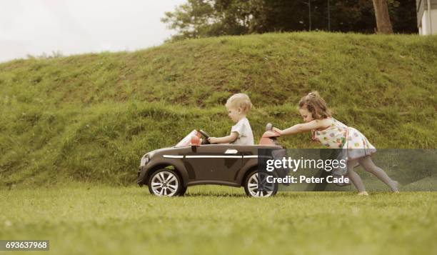 girl pushing little brother in toy car - empujar fotografías e imágenes de stock