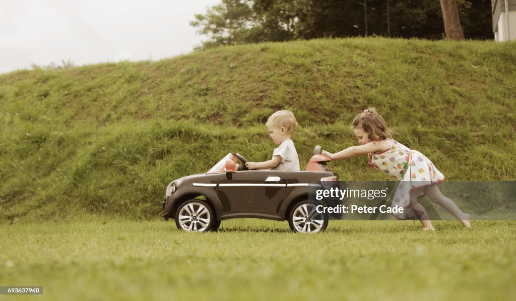 Girl pushing little brother in toy car
