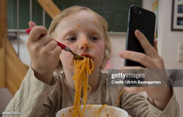 Young people and the dependence on electronic media. The photo shows a young girl during her spaghetti meal - completely distracted and fascinated by...