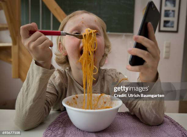 Young people and the dependence on electronic media. The photo shows a young girl during her spaghetti meal - completely distracted and fascinated by...