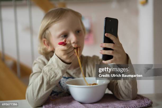 Young people and the dependence on electronic media. The photo shows a young girl during her spaghetti meal - completely distracted and fascinated by...