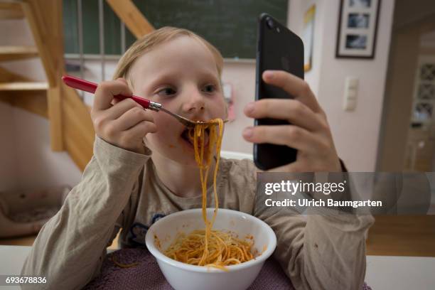 Young people and the dependence on electronic media. The photo shows a young girl during her spaghetti meal - completely distracted and fascinated by...