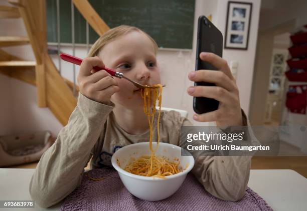 Young people and the dependence on electronic media. The photo shows a young girl during her spaghetti meal - completely distracted and fascinated by...