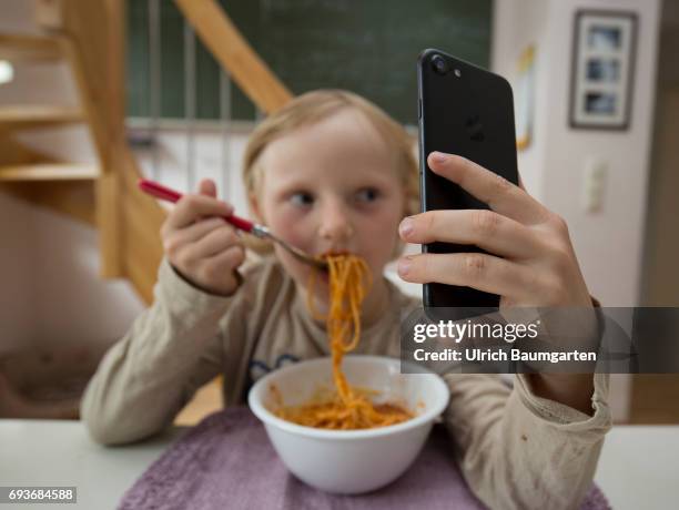 Young people and the dependence on electronic media. The photo shows a young girl during her spaghetti meal - completely distracted and fascinated by...