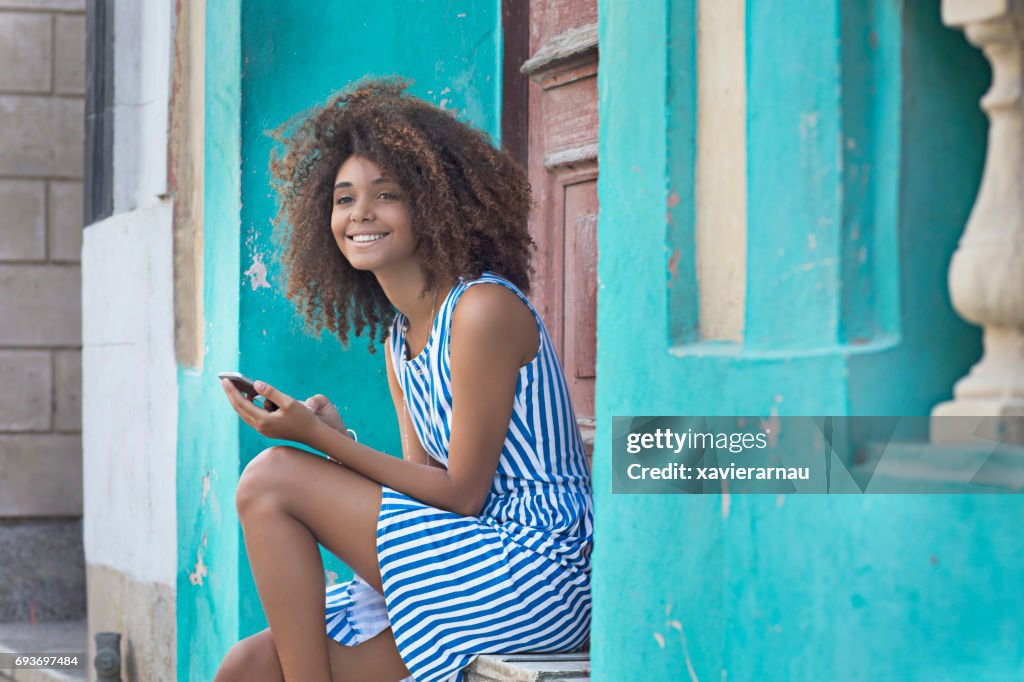 Woman using mobile phone while sitting at entrance