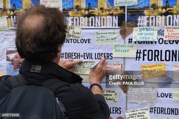 Man adds a messagesof solidarity written on post-it notes stuck to a wall at the southern end of London Bridge in London on June 8, 2017 following...