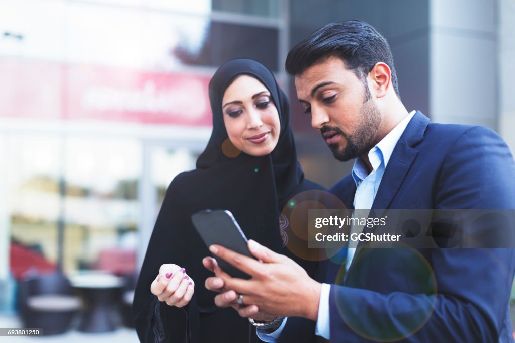 Modern Arab husband showing his wife an online message on his smart phone