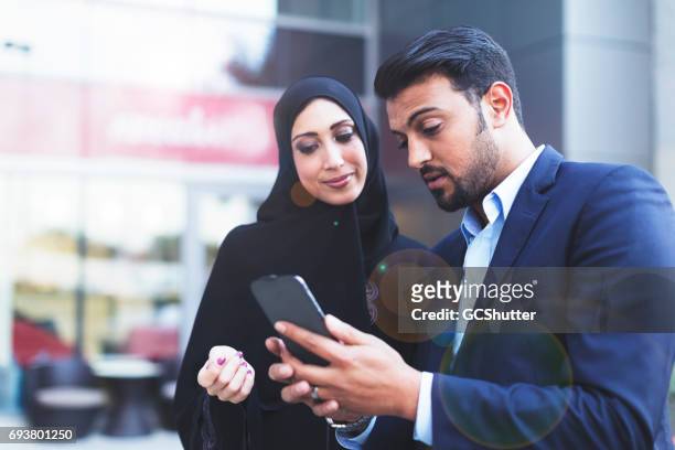 modern arab husband showing his wife an online message on his smart phone - arabic style stock pictures, royalty-free photos & images
