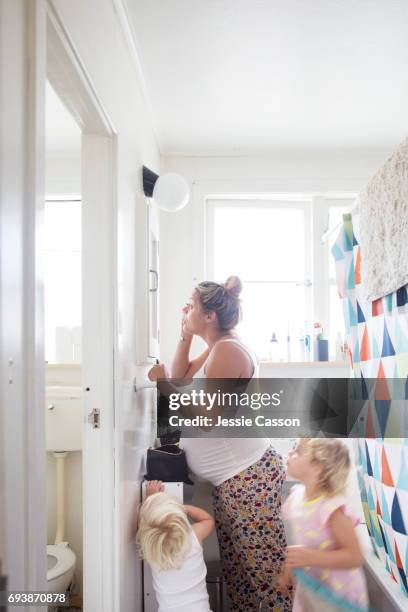 pregnant mother puts on makeup in bathroom with two small children around her - busy mum mess stock-fotos und bilder