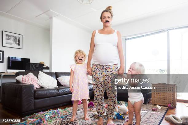 pregnant mother and two children wearing moustaches in messy living room - 5 funny foto e immagini stock