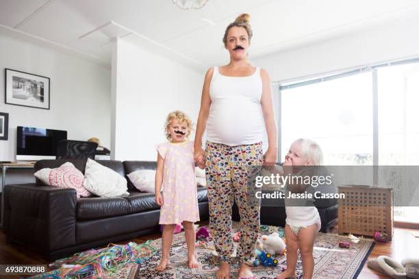 pregnant mother and two children wearing moustaches in messy living room - offbeat imagens e fotografias de stock