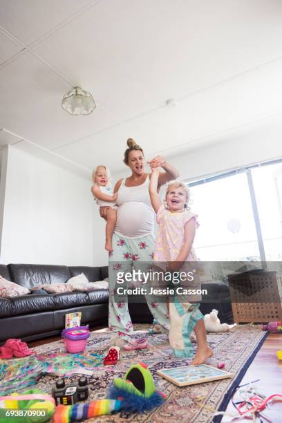 pregnant mother in pyjamas dancing with two children in messy house - kids mess carpet stock pictures, royalty-free photos & images