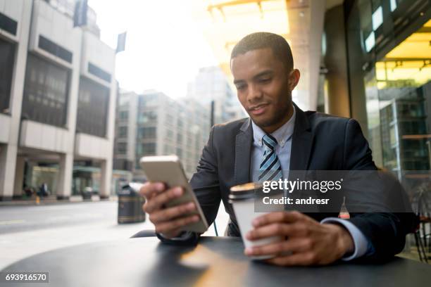 jonge business man sms op zijn telefoon in een café - african american restaurant texting stockfoto's en -beelden