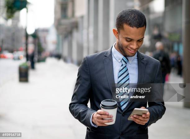 young business man texting on his phone and drinking coffee - man atm smile stock pictures, royalty-free photos & images
