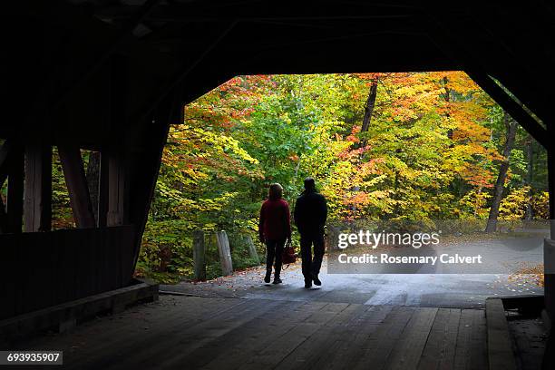 couple leave covered bridge with trees in autumn - autumn covered bridge stock pictures, royalty-free photos & images