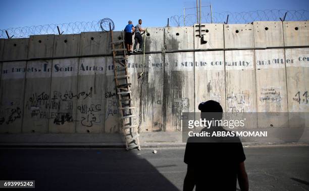 Man watches as Palestinian youths attempt to cross over the separation barrier using a ladder next to Qalandia checkpoint in the occupied West Bank...