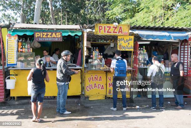 Cuban real people selling and buying pizzas close to the Medicine school. People purchasing food and drinks from private small roadside kiosks.