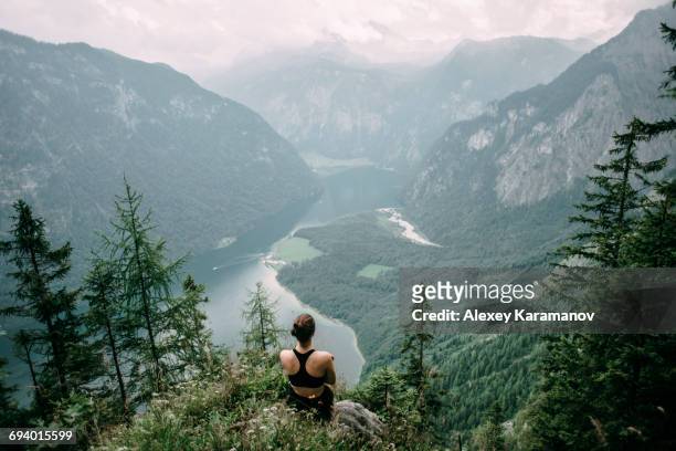 caucasian woman sitting on rock overlooking lake in valley - über etwas schauen stock-fotos und bilder