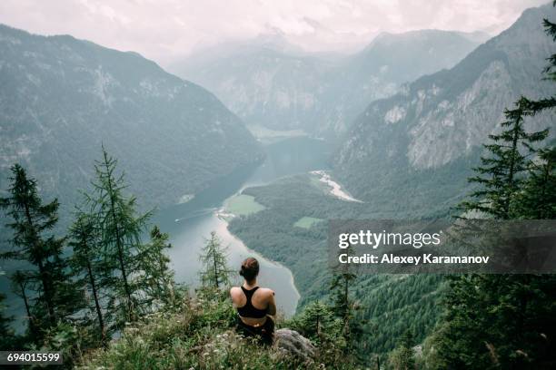 caucasian woman sitting on rock overlooking lake in valley - ergens overheen kijken stockfoto's en -beelden