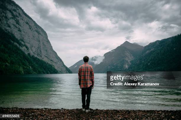 caucasian man standing near mountain lake - rückansicht stock-fotos und bilder