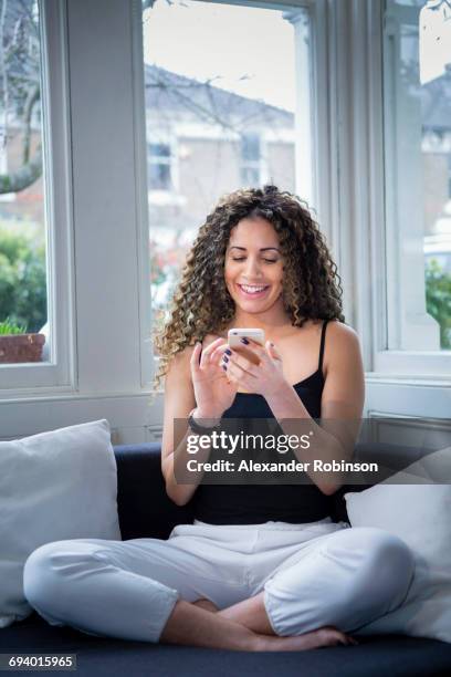 smiling woman sitting near window texting on cell phone - jogging pants 個照片及圖片檔