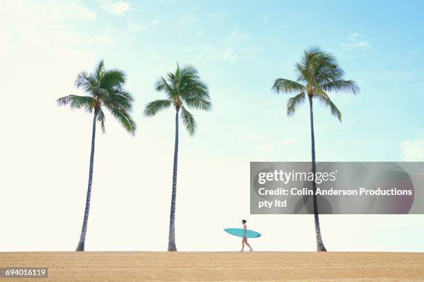 pacific islander woman carrying surfboard walking near palm tree - palm sunday stockfoto's en -beelden