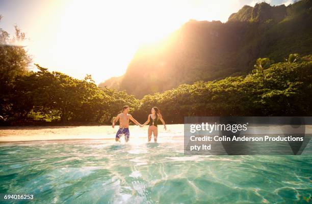 couple holding hands running into ocean - hawaii fun stock-fotos und bilder