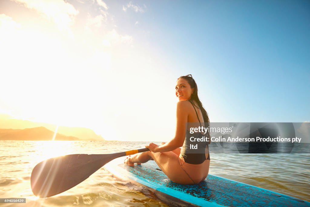 Mixed Race woman sitting on paddleboard in ocean