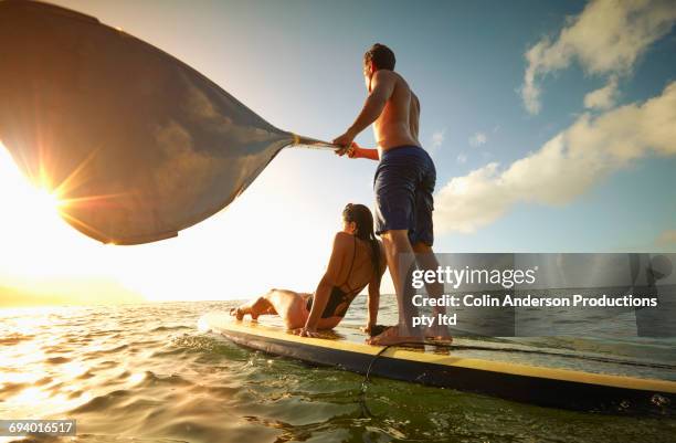 couple on paddleboard in ocean at sunset - frau sommer natur bewegung freude sport stock-fotos und bilder