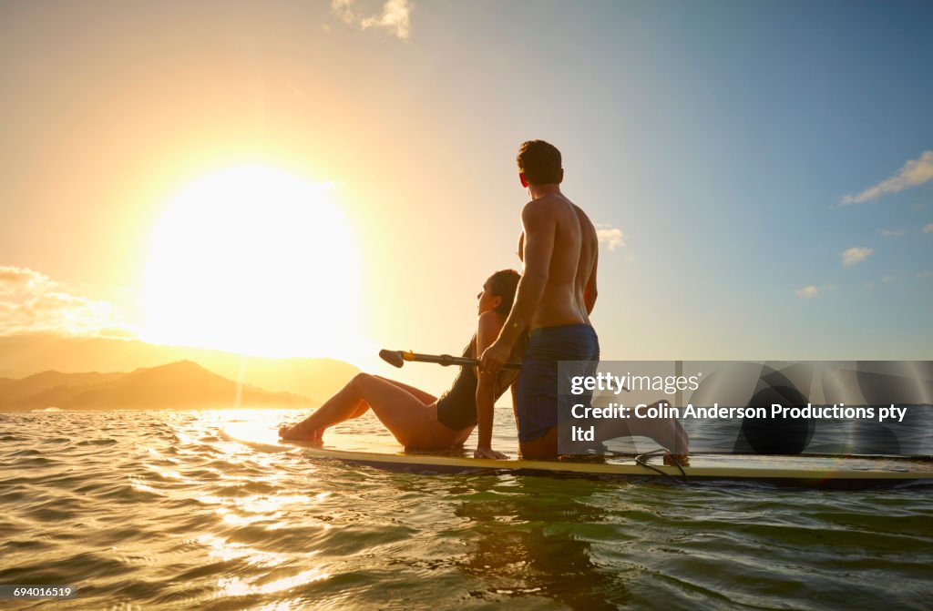 Couple on paddleboard in ocean at sunset