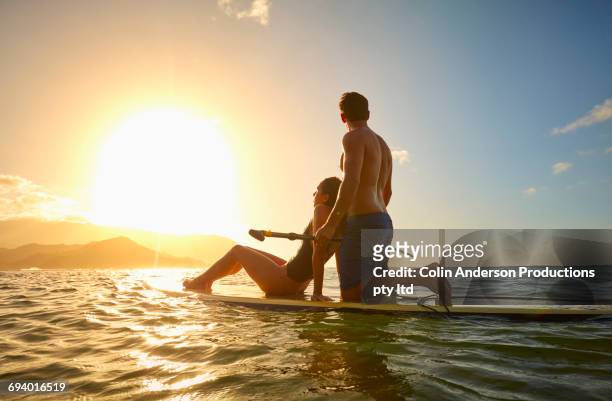 couple on paddleboard in ocean at sunset - girlfriend getaway stock pictures, royalty-free photos & images