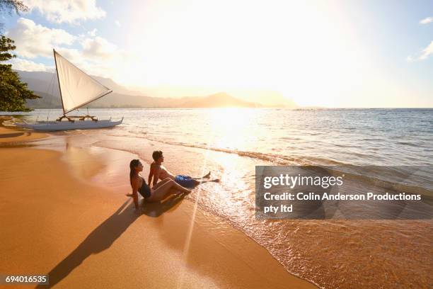 couple sitting on beach near sailboat - couple voyage sport photos et images de collection