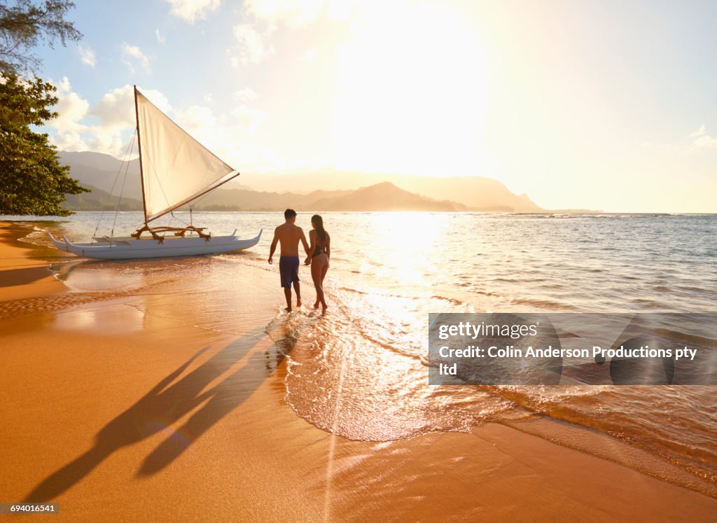 Couple walking on beach near sailboat