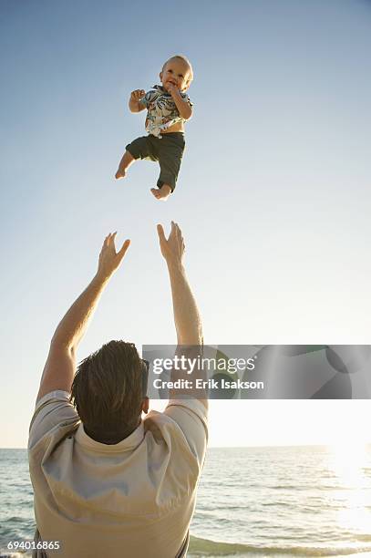 caucasian father throwing baby son in air near ocean - boy in wind stock-fotos und bilder