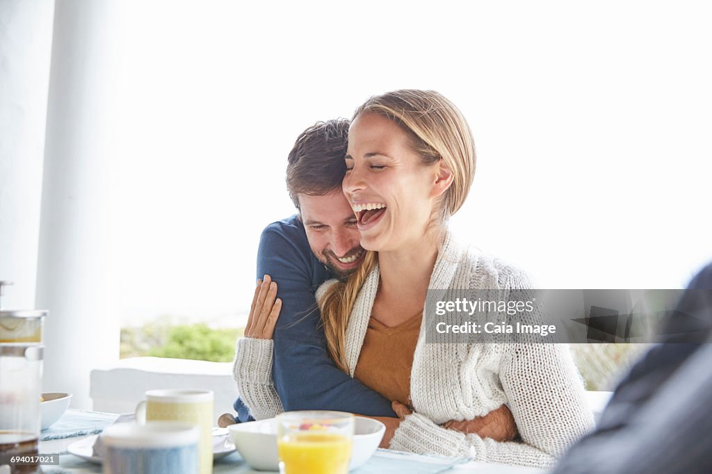 Affectionate couple hugging and laughing at breakfast on patio