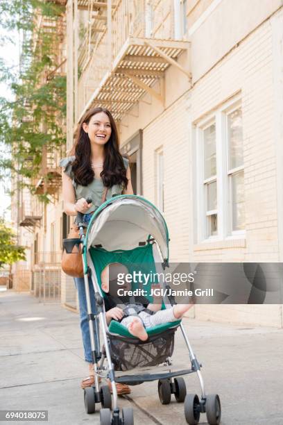 mother pushing baby son in stroller in city - mum pushing pram stock-fotos und bilder