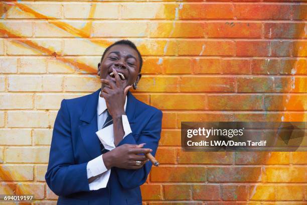 laughing androgynous black woman leaning on mural smoking cigar - black transgender 個照片及圖片檔